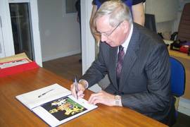 The Duke of Gloucester sitting down and signing a booklet.